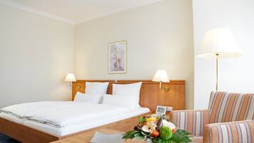 A hotel room with a neatly made bed, two bedside lamps, a wooden headboard, a small table with a vase of flowers, and a striped armchair.