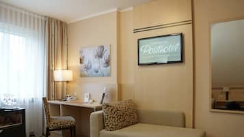 Habitación de hotel con escritorio, dos sillas, sofá, televisión y un cuadro en la pared.