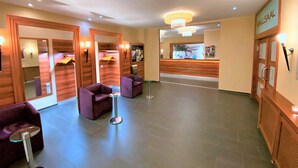 A hotel lobby with a reception desk, two purple armchairs, a small round table, and a chandelier. - Hünerbein's Posthotel (Bissendorf)