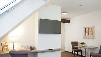 A modern room with a desk, chairs, a flat-screen TV, a painting, and a window with a view.