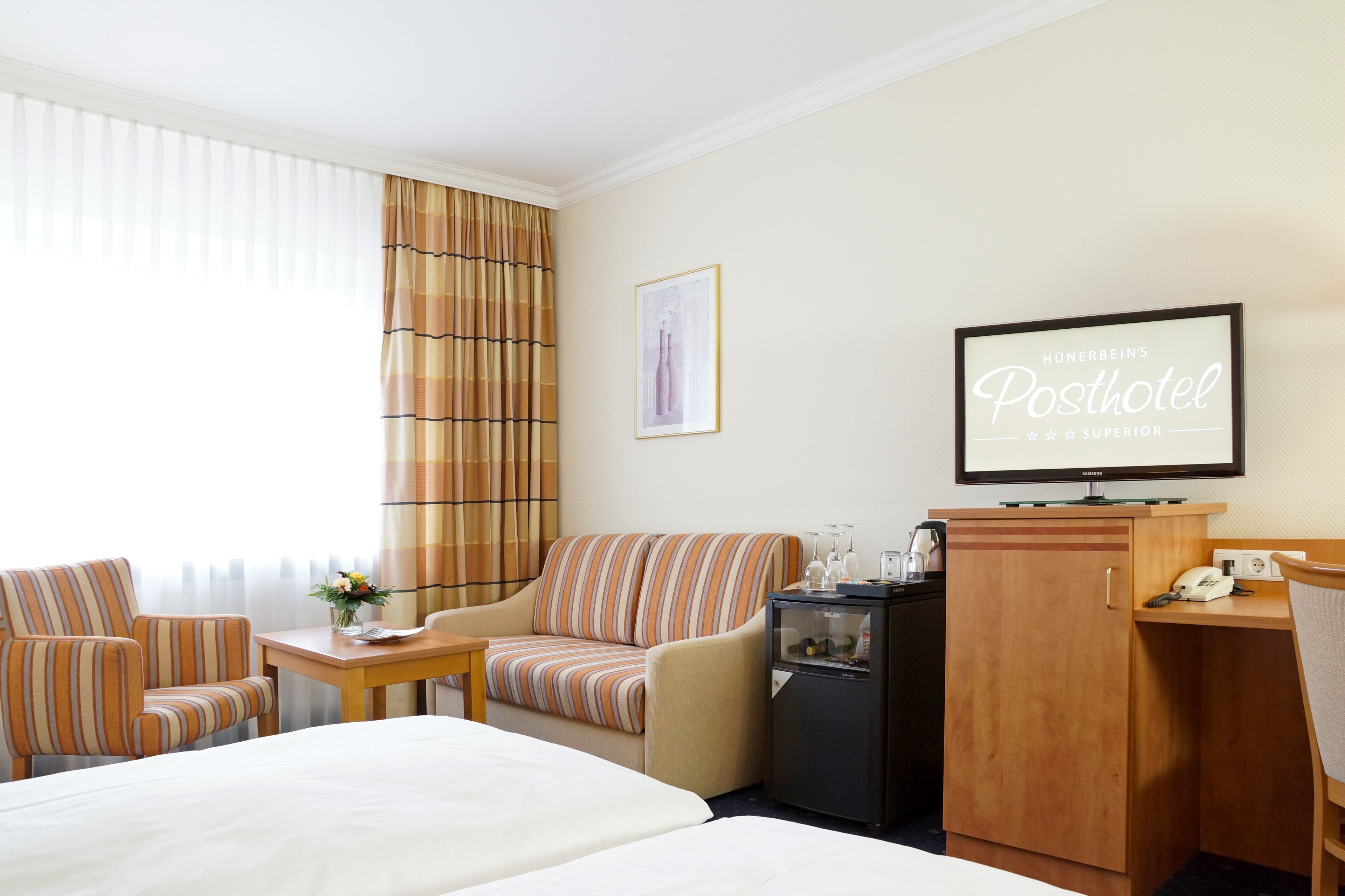 A hotel room with a bed, a sofa, a desk, a television, and a minibar.