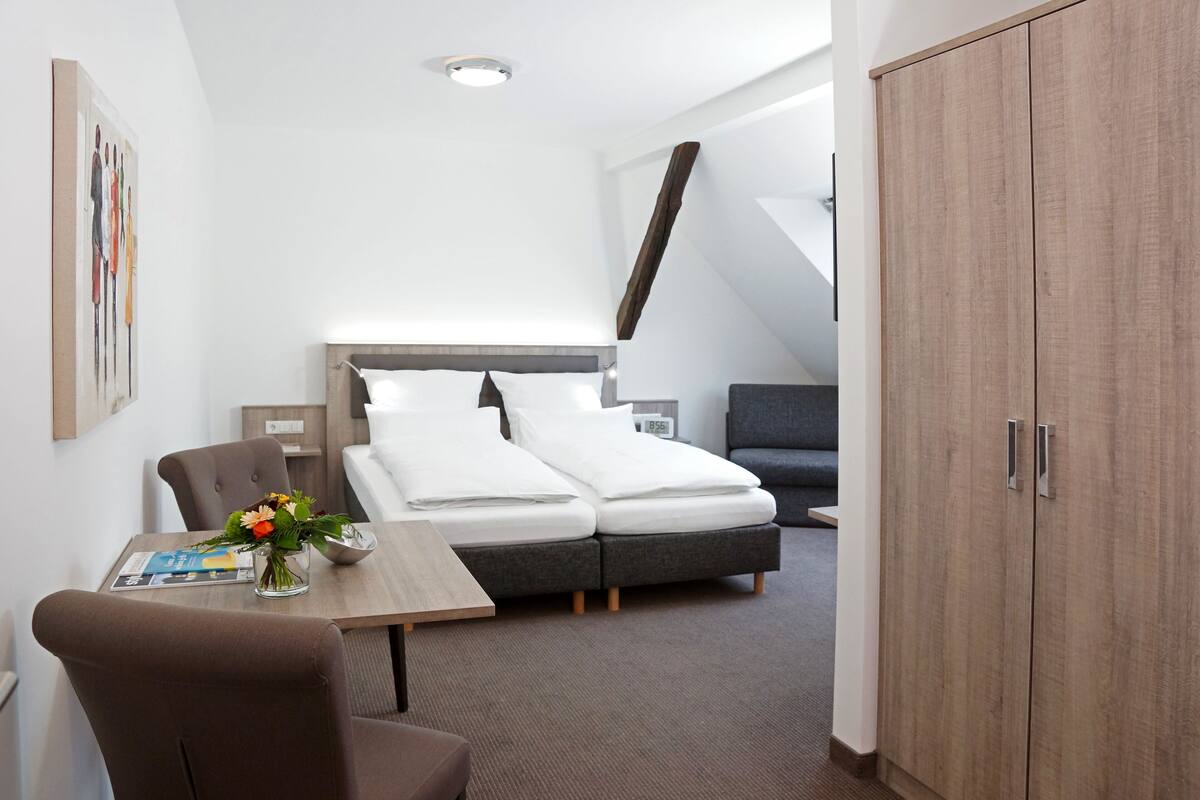 Una habitación de hotel moderna con una cama, un escritorio, una silla, un armario y un cuadro en la pared.