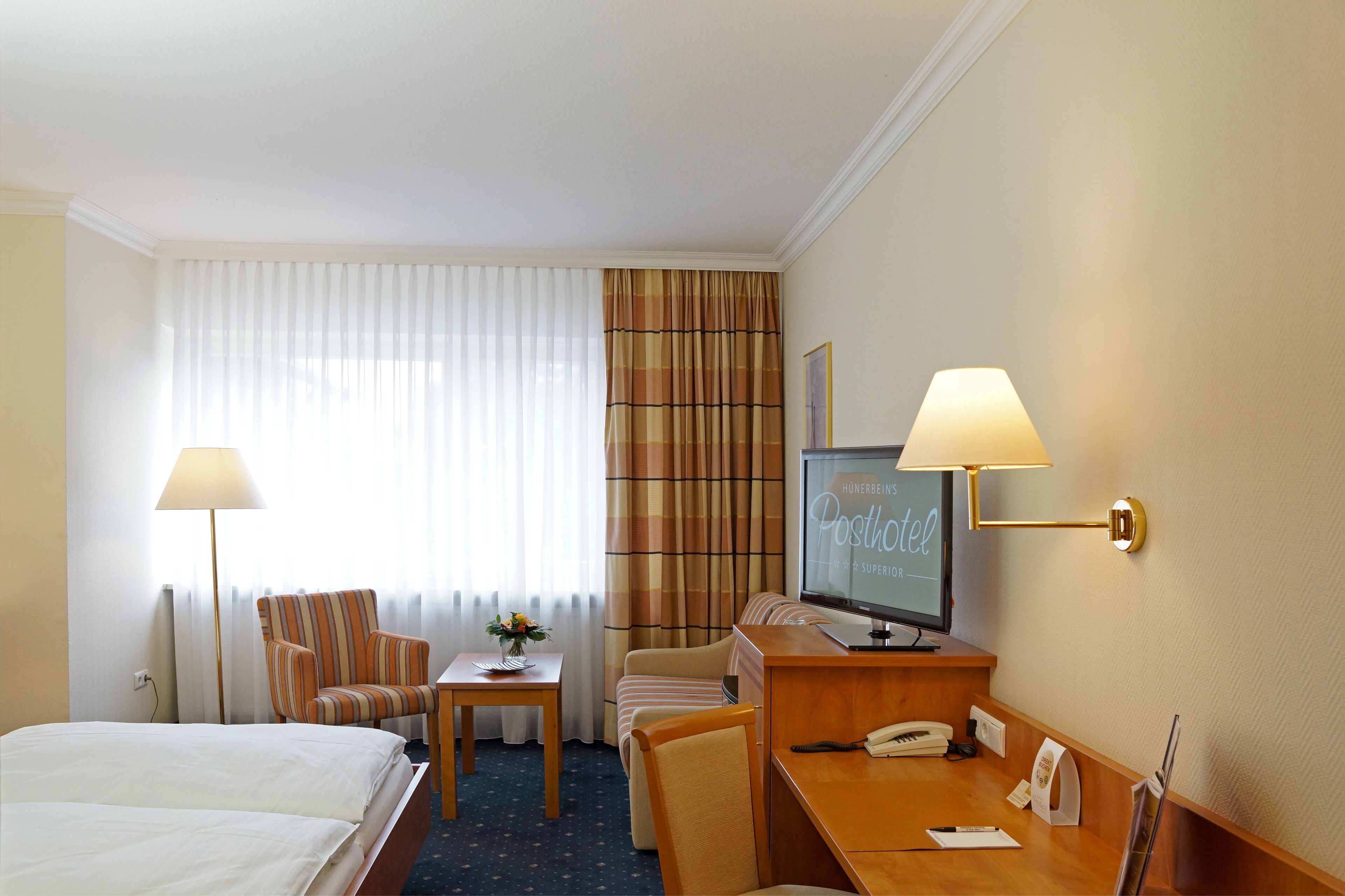 Une chambre d’hôtel avec un lit, deux chaises, un bureau, une télévision et une lampe.