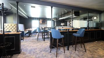 Zona de bar moderna con taburetes altos, barra y área de estar con mesas y sillas.