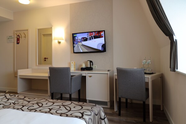 A hotel room with a bed, a desk, two chairs, a television, and a window with curtains. - Hotel Märkischer Hof (Luckenwalde)