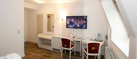 A hotel room with a bed, a desk, two chairs, a television, and a window.