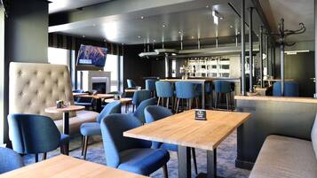 A modern restaurant with high tables, blue chairs, and a bar area.