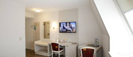 A hotel room with a desk, two chairs, a television, and a window.