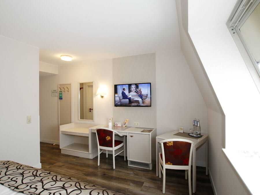 Ein Hotelzimmer mit Schreibtisch, zwei Stühlen, Fernseher und Fenster.