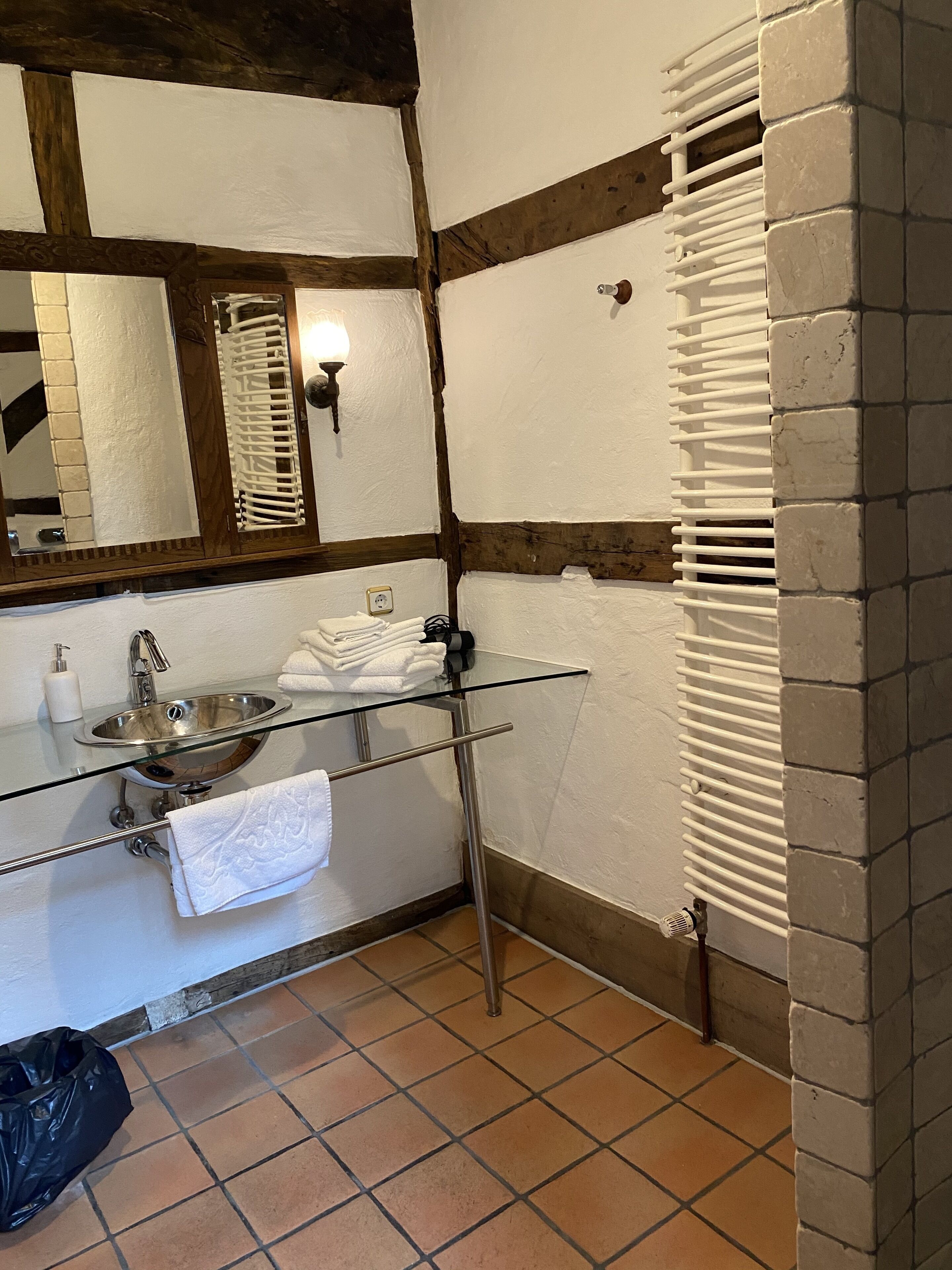 A bathroom with a glass sink, white tiles, a towel rack, and a mirror.