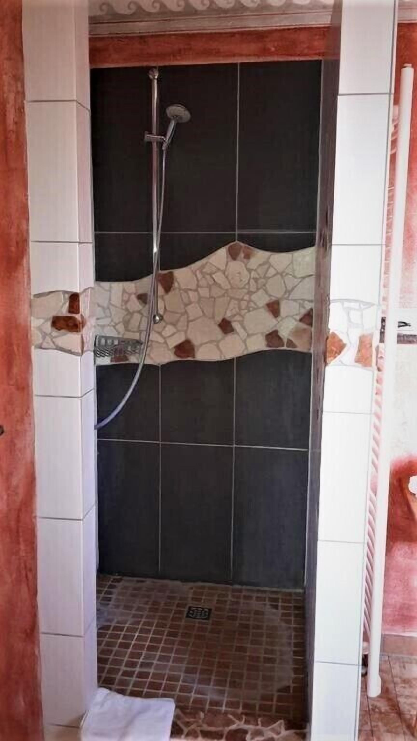 Um chuveiro com parede revestida de azulejos, um espalhador e um ralo.