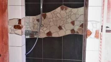 Um chuveiro com parede revestida de azulejos, um espalhador e um ralo.