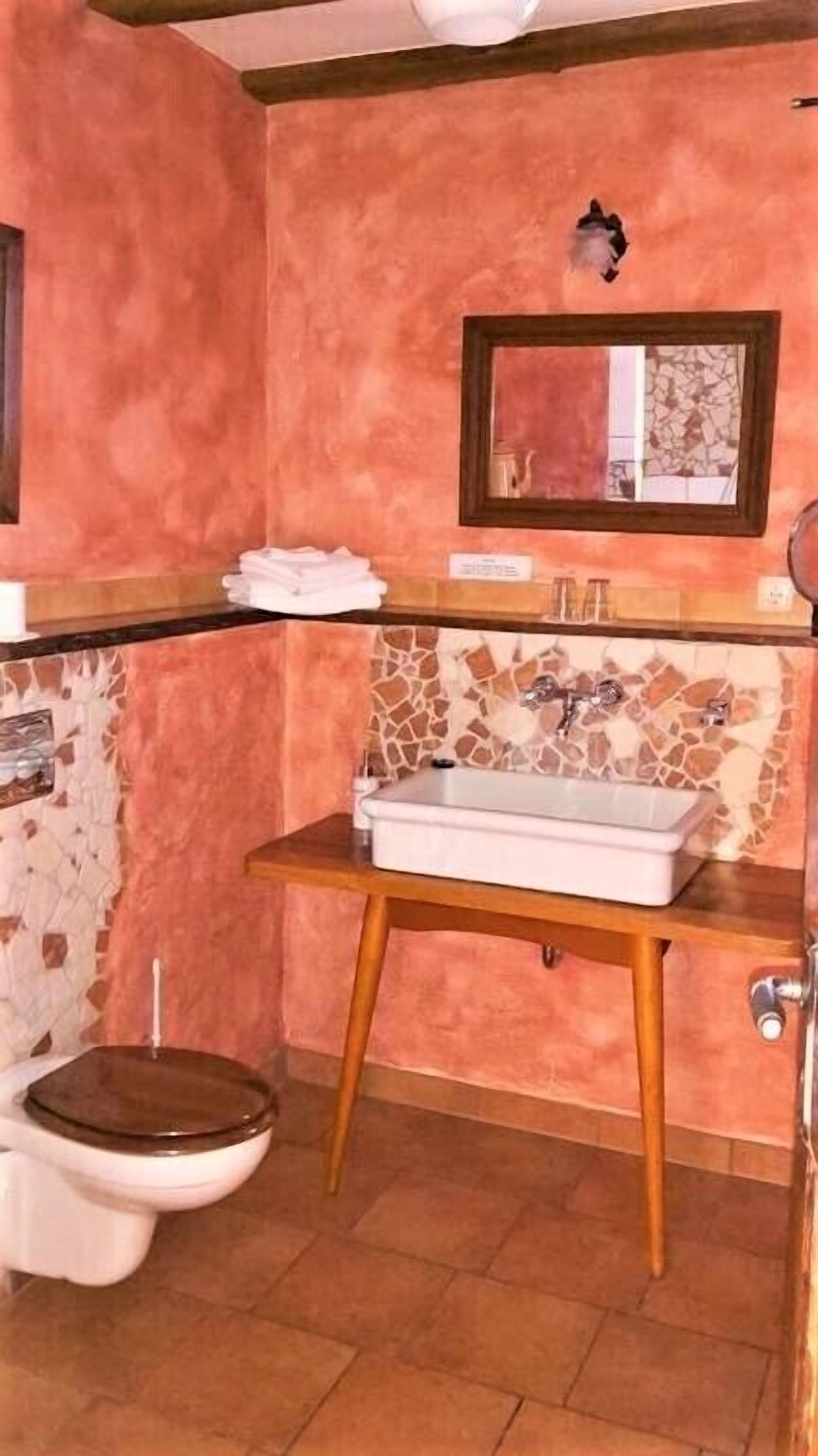 Ein Badezimmer mit einem Holzkosmetikschrank, einem weißen Waschbecken, einer Toilette und einer Mosaikrückwand.
