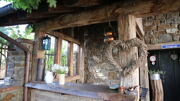 A rustic wooden bar area with a stone wall backdrop, a hanging copper pot, and a sign reading "Eingang" (entrance). - Historische Wassermühle (Birgel)