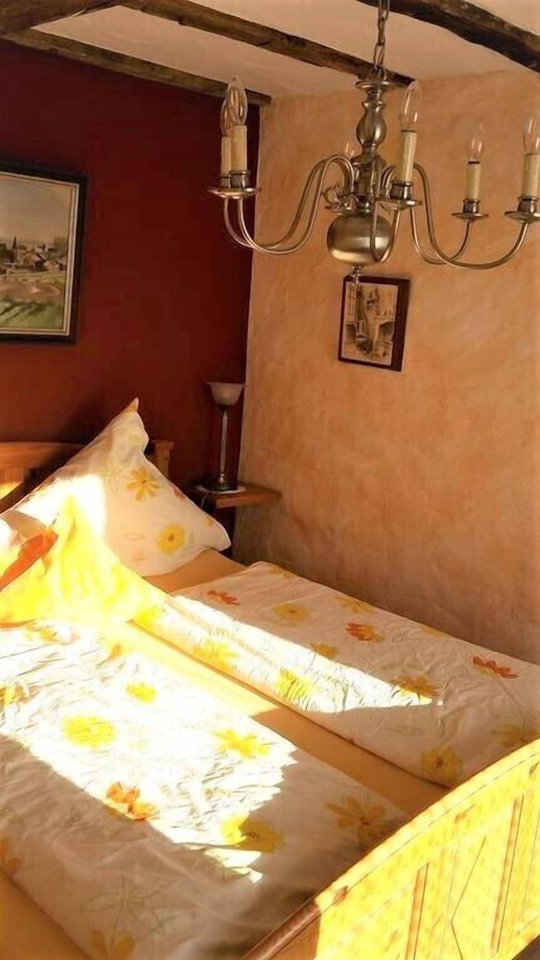 A room with a bed, a chandelier, and a painting on the wall.