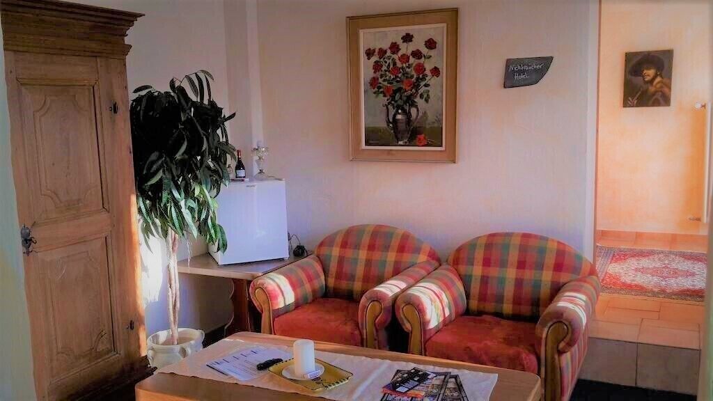 A living room with a wooden cabinet, a table with papers, a potted plant, a sofa with plaid cushions, a framed painting of flowers, and a sign that says "McGregor Hotel".
