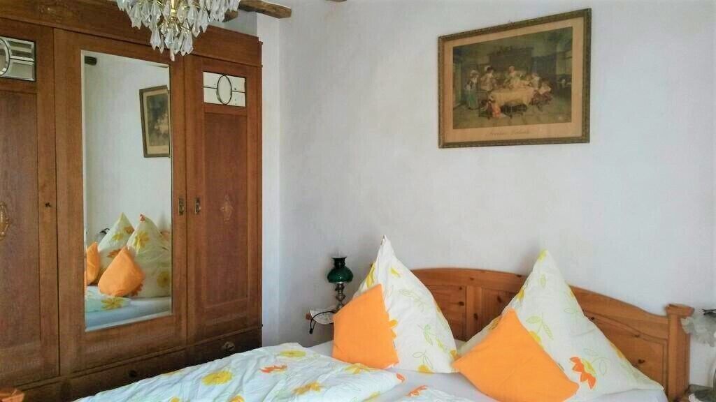Un dormitorio con un armario de madera, una cama con almohadas anaranjadas y blancas, una lámpara verde y un cuadro enmarcado en la pared.