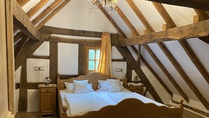 A bedroom with a wooden bed, a nightstand, a lamp, and a window with curtains. - Historische Wassermühle (Birgel)
