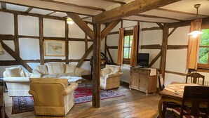 A cozy living room with wooden beams, a television, and a dining area with a table and chairs. - Historische Wassermühle (Birgel)