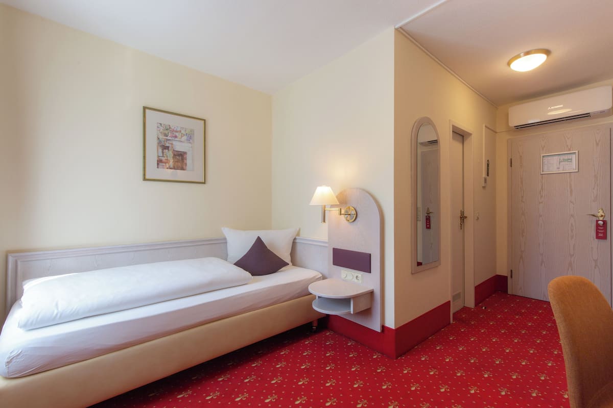 Habitación de hotel con cama, mesita de noche, lámpara, espejo y alfombra roja.
