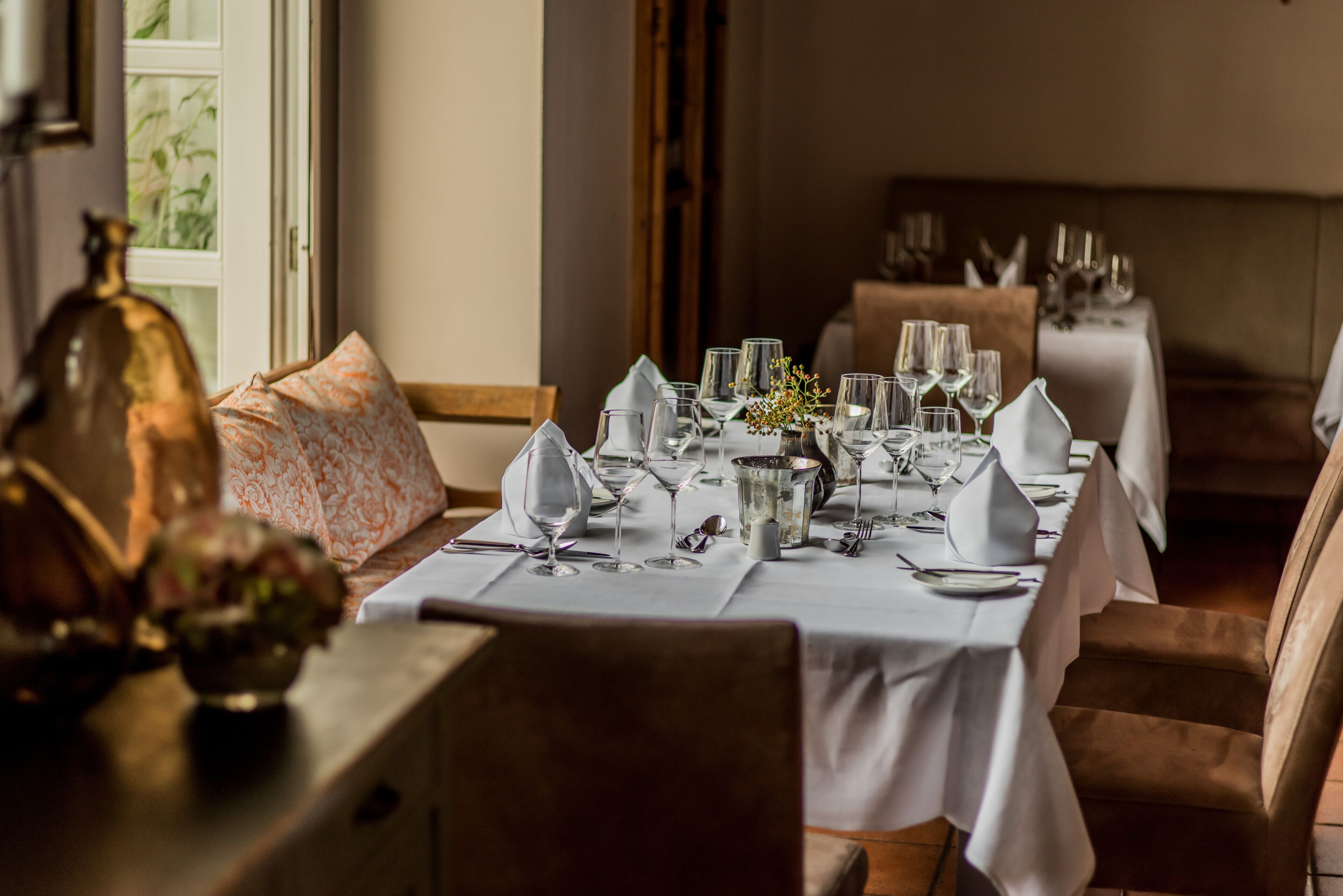 A dining table set with white tablecloths, silverware, and wine glasses, with a vase of flowers on the table.