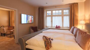 Habitación de hotel con una cama grande, un televisor en la pared, una ventana con cortinas, una silla y una lámpara.