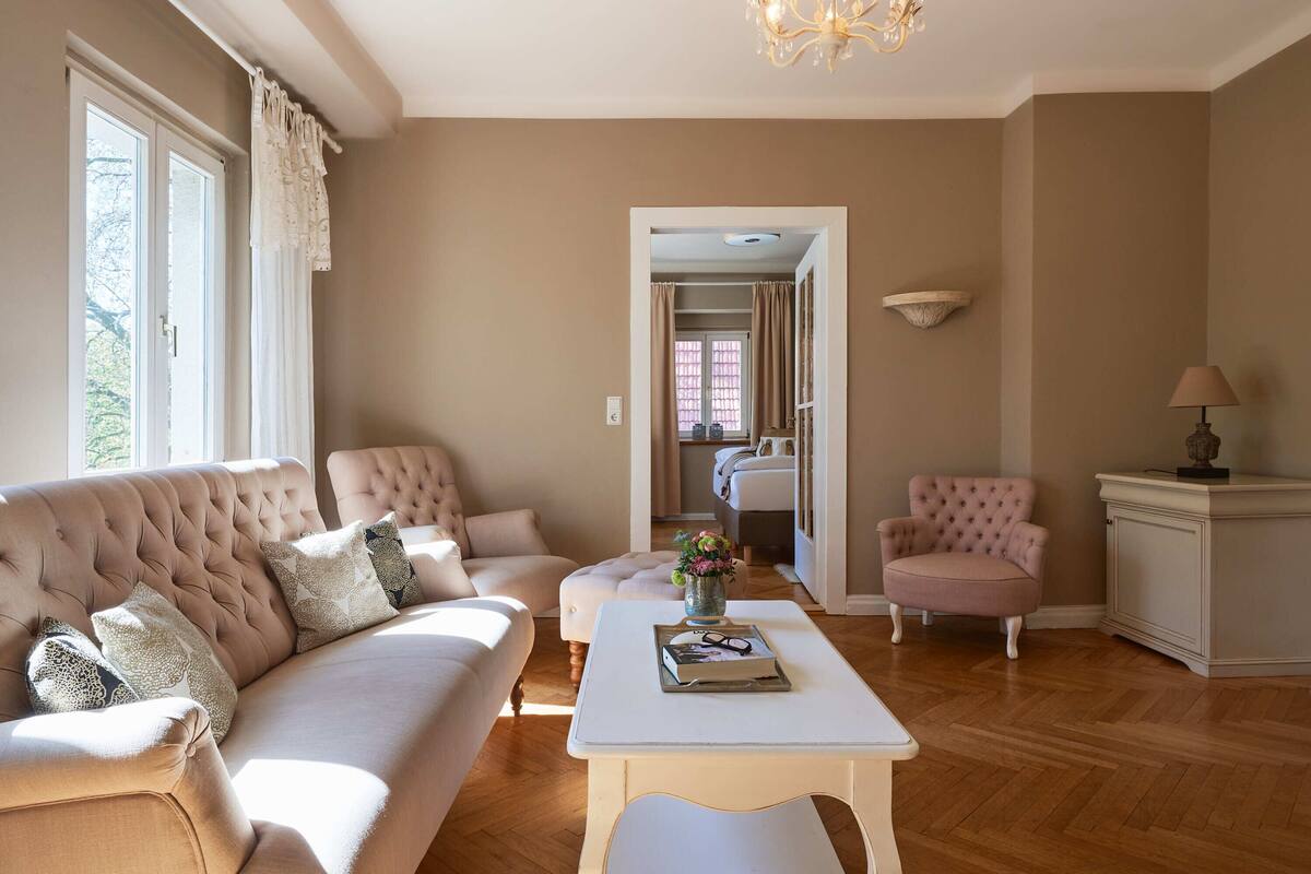 A living room with a beige sofa, a white coffee table, and a pink armchair.