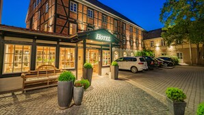 Un hotel europeo tradicional con un patio adoquinado, un banco de madera y un aparcamiento.