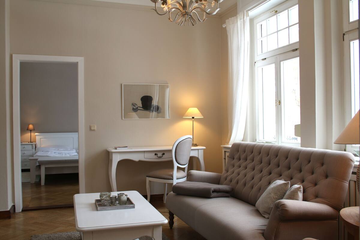 A well-lit room with a bed, a desk, a chair, a sofa, and a lamp.