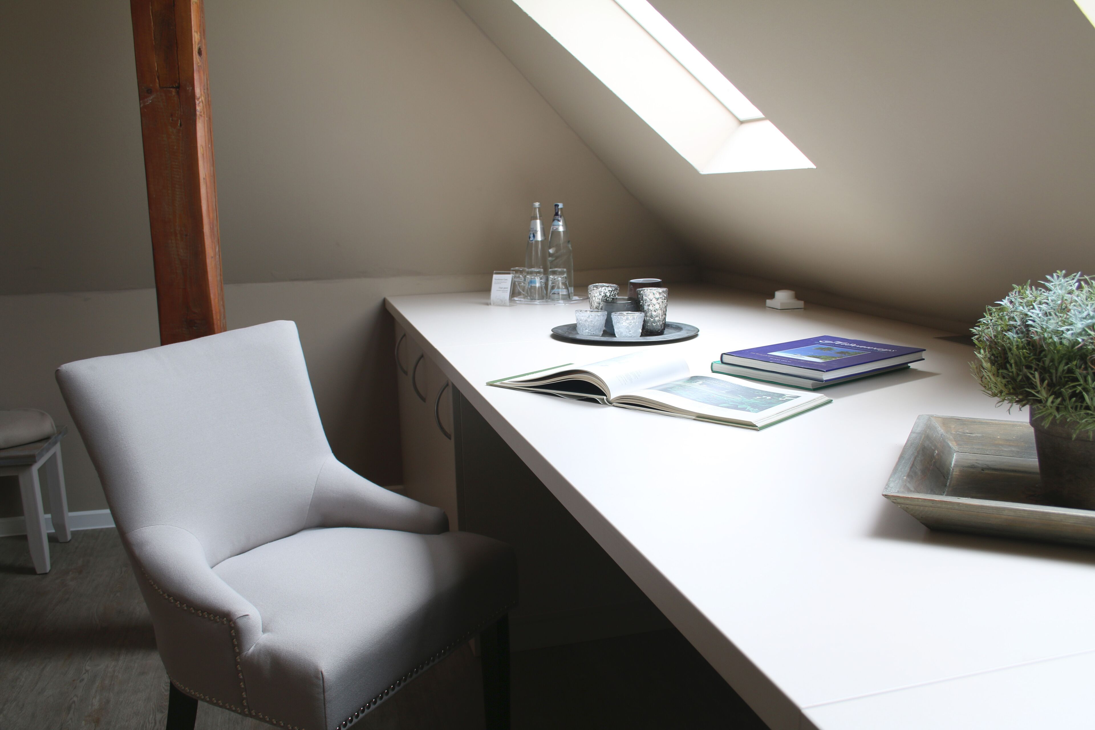 Ein Zimmer mit weißem Schreibtisch, einem Stuhl, einem Oberlicht und einem Blumentopf.