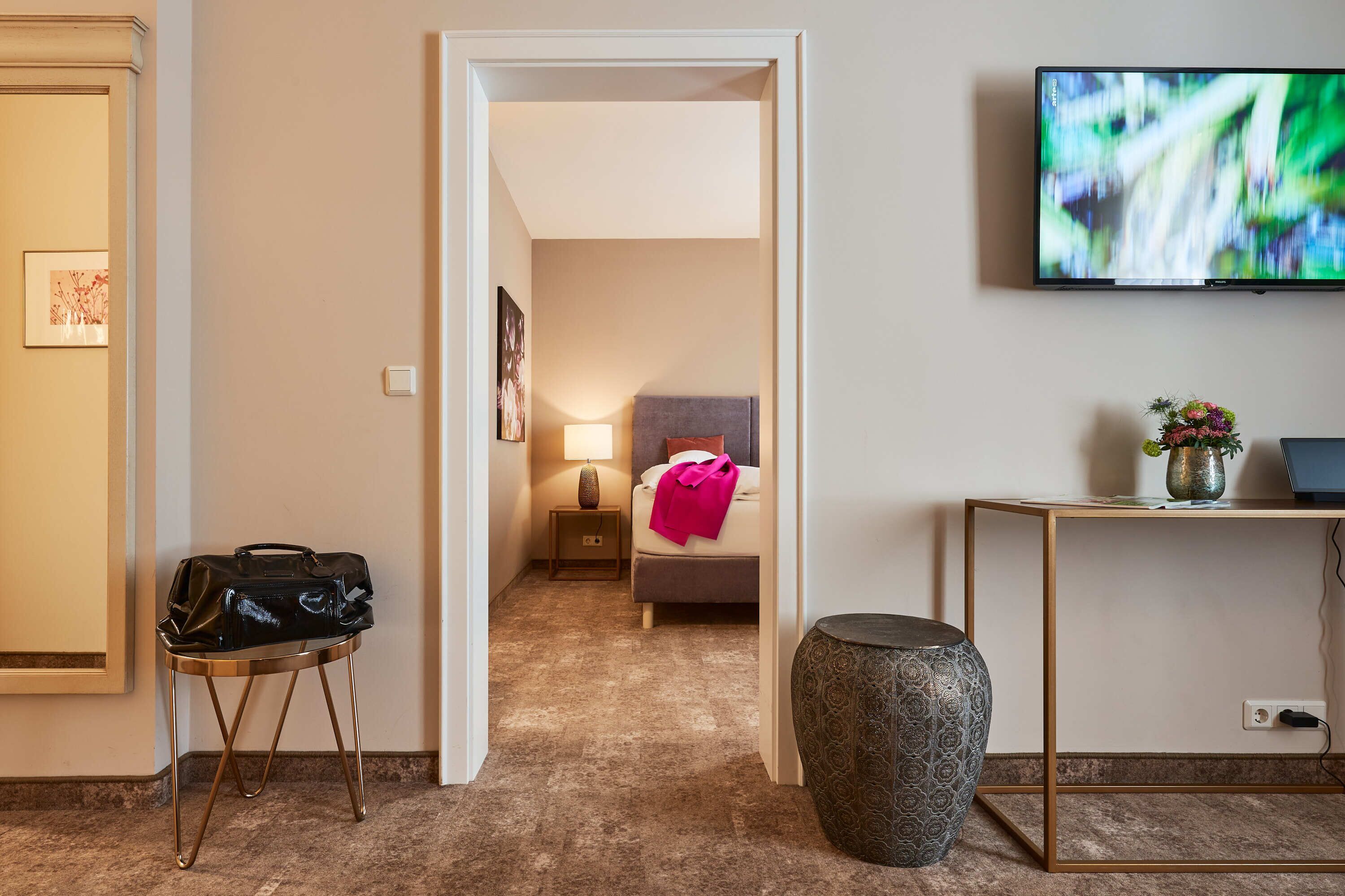 Habitación de hotel con cama, mesita de noche, lámpara, televisión y una pequeña mesa con un florero.