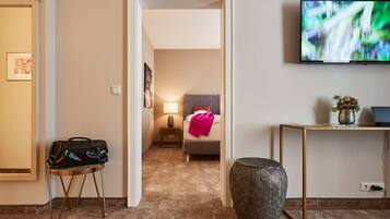 Habitación de hotel con cama, mesita de noche, lámpara, televisión y una pequeña mesa con un florero.