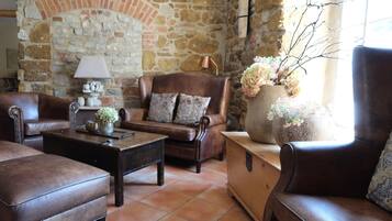 A cozy living room with a stone wall, leather furniture, and a large vase with flowers.