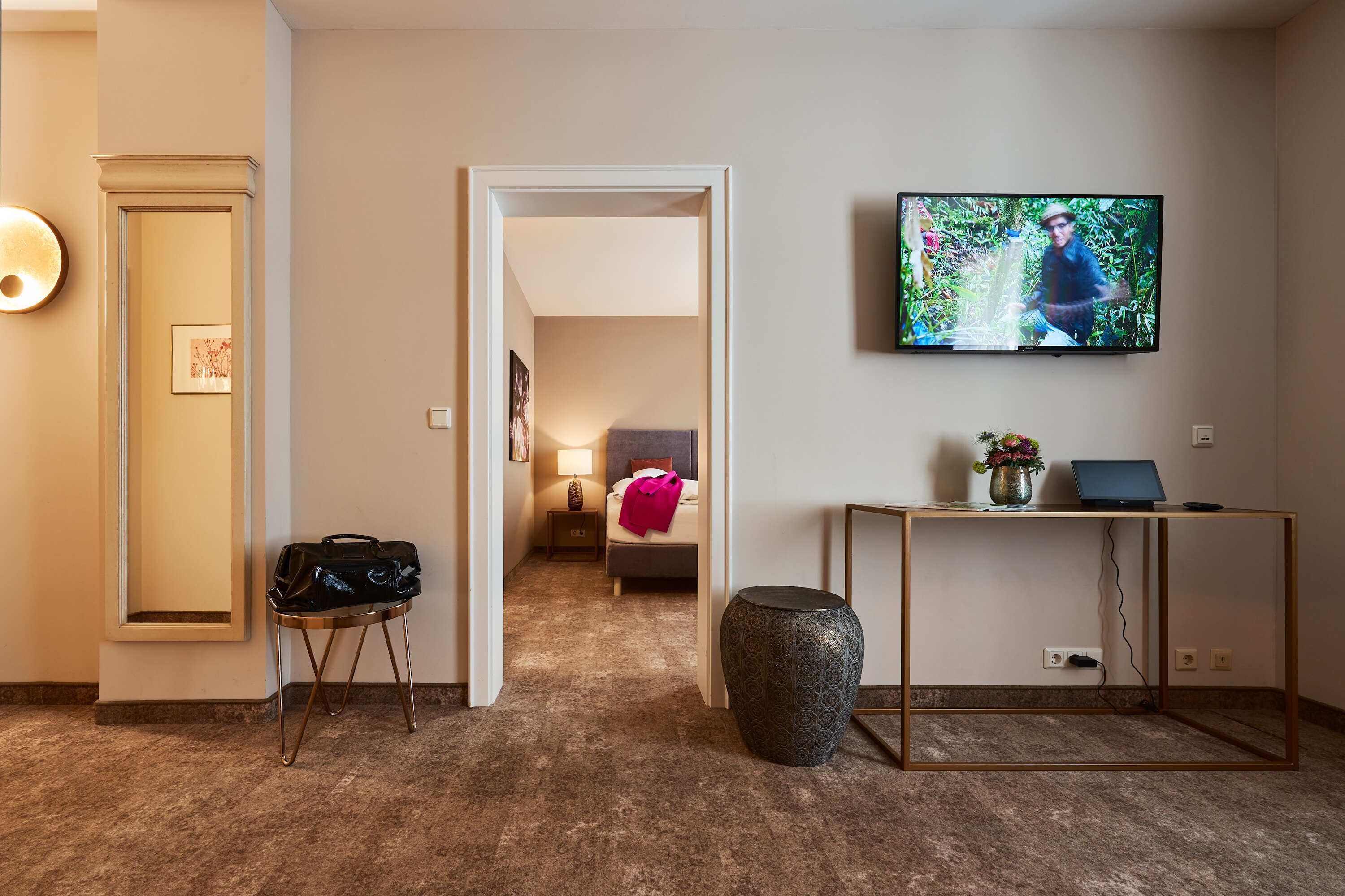 A hotel room with a bed, a TV, a desk, and a suitcase on a stand.