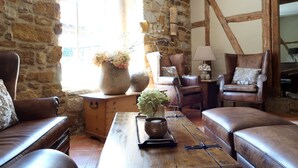 Una habitación acogedora con paredes de piedra, vigas de madera, mobiliario de cuero y un amplio ventanal con luz natural.