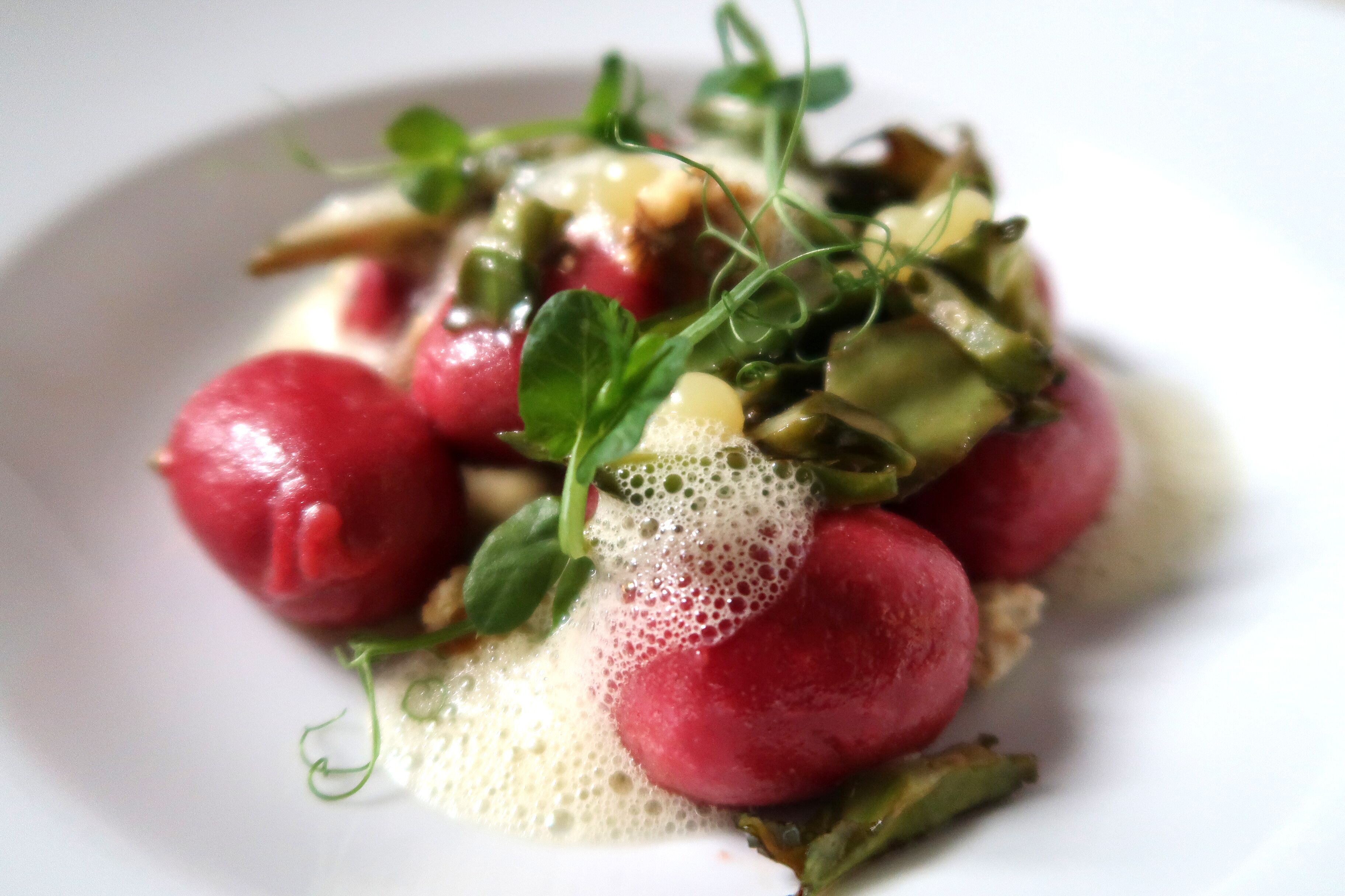 A plate with a dish of radishes, greens, and a creamy sauce.