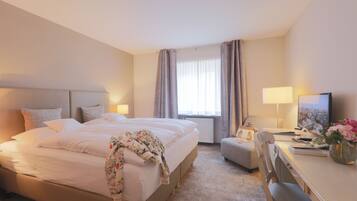 Habitación de hotel con una cama grande, un escritorio con silla, televisor y ventana con cortinas.