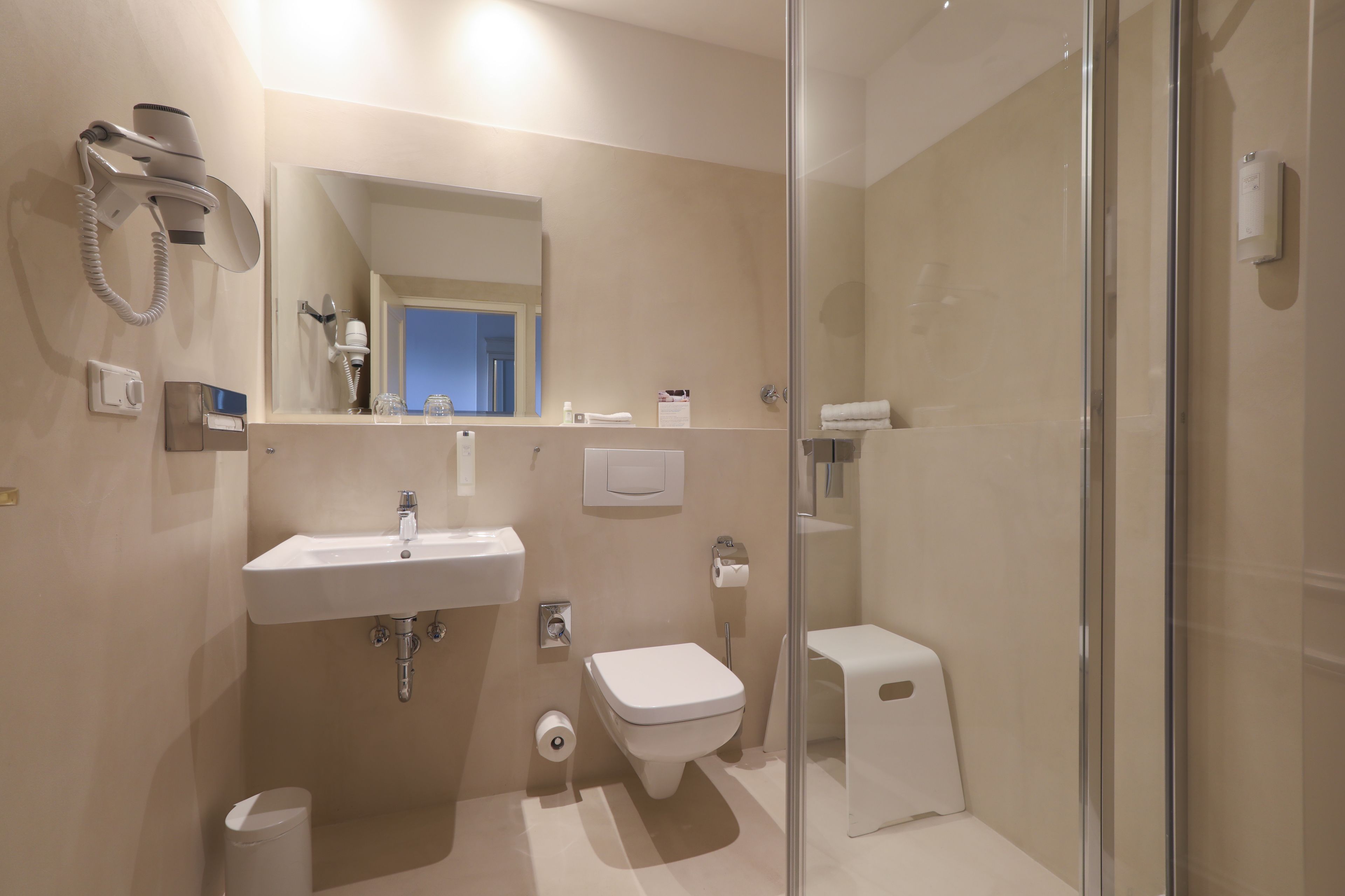 Une salle de bain moderne avec une douche à parois de verre, un lavabo, des toilettes et un sèche-cheveux fixé au mur.