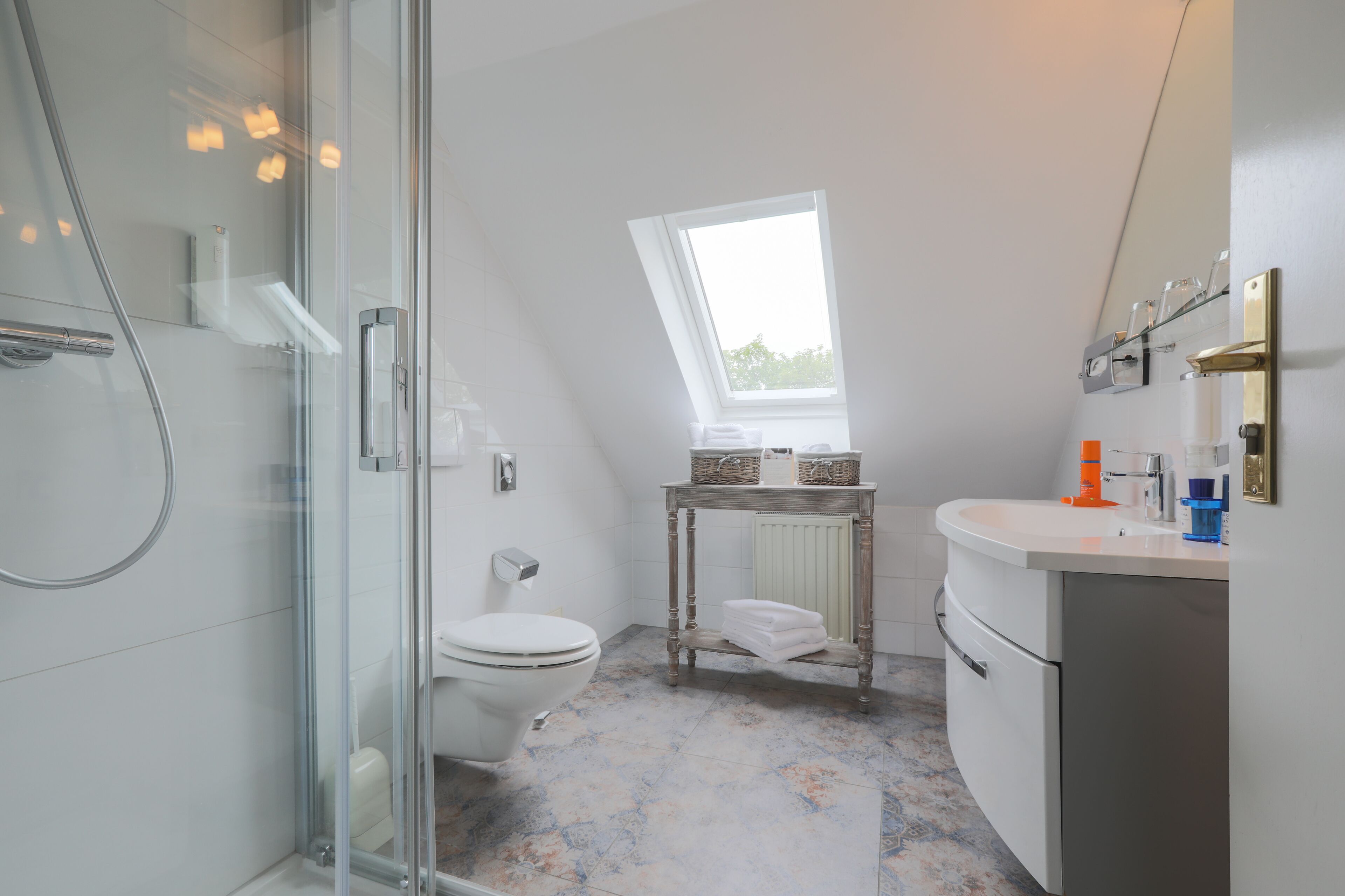 A modern bathroom with a glass shower enclosure, a toilet, a sink with a mirror, and a small table with baskets.