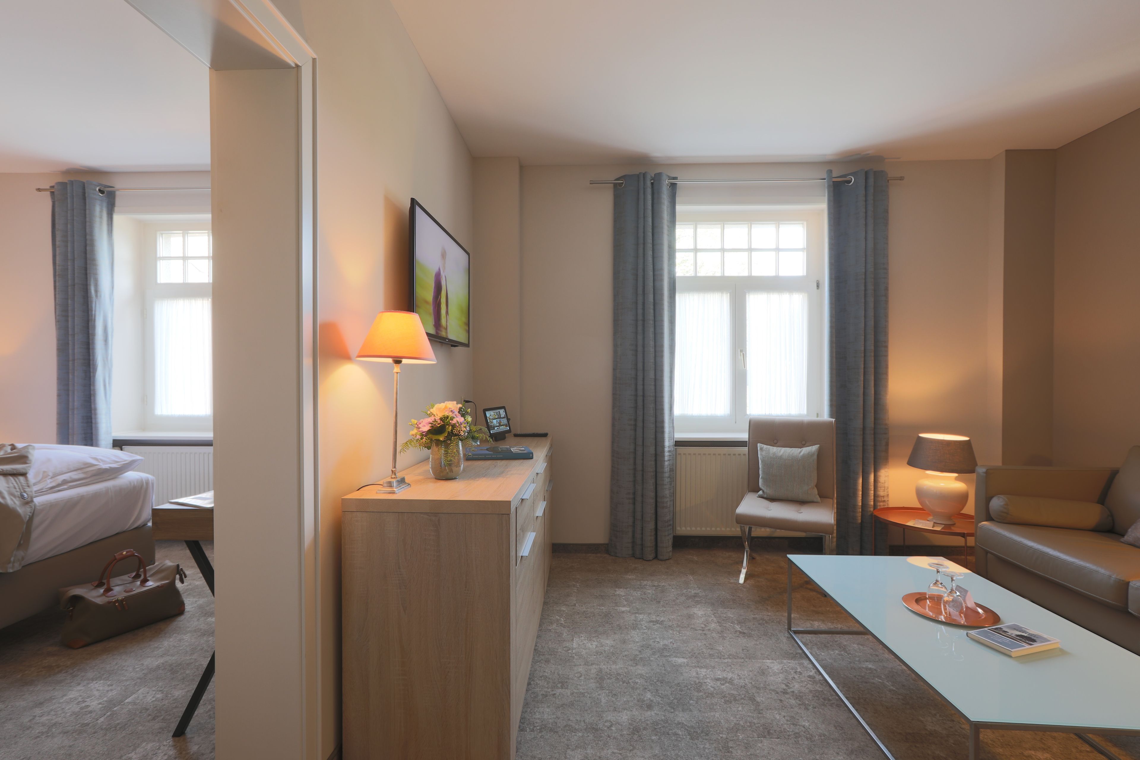 Une chambre d’hôtel moderne équipée d’un lit, d’un bureau, d’une chaise, d’un canapé et offrant une vue sur l’extérieur grâce à de grandes fenêtres.