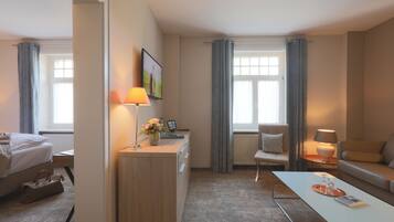Une chambre d’hôtel moderne équipée d’un lit, d’un bureau, d’une chaise, d’un canapé et offrant une vue sur l’extérieur grâce à de grandes fenêtres.