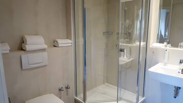 Un baño moderno con ducha de vidrio, un lavabo blanco y toallas ordenadas sobre una repisa.