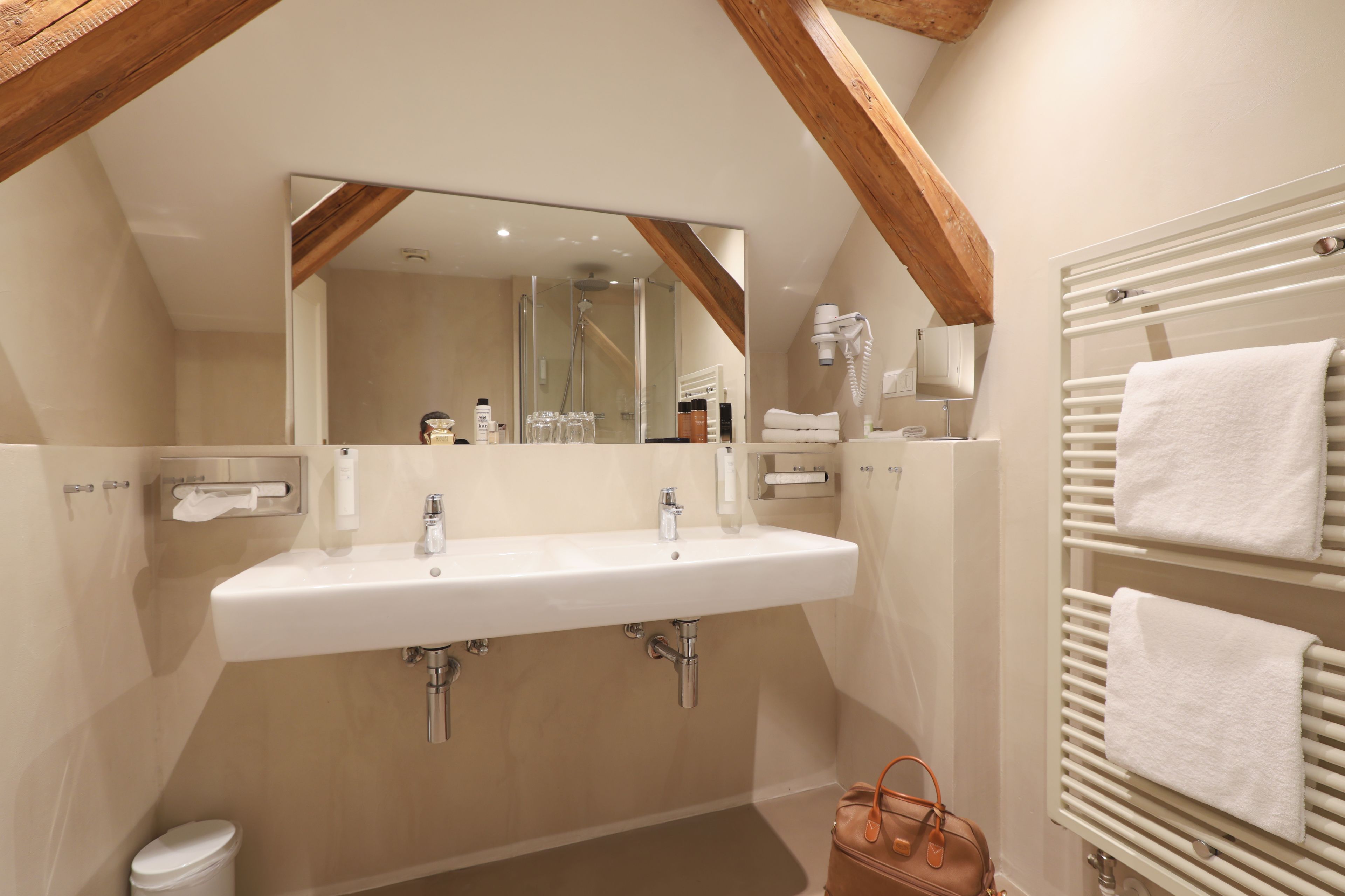 A bathroom with a large mirror, a sink, a towel rack, and a shower.