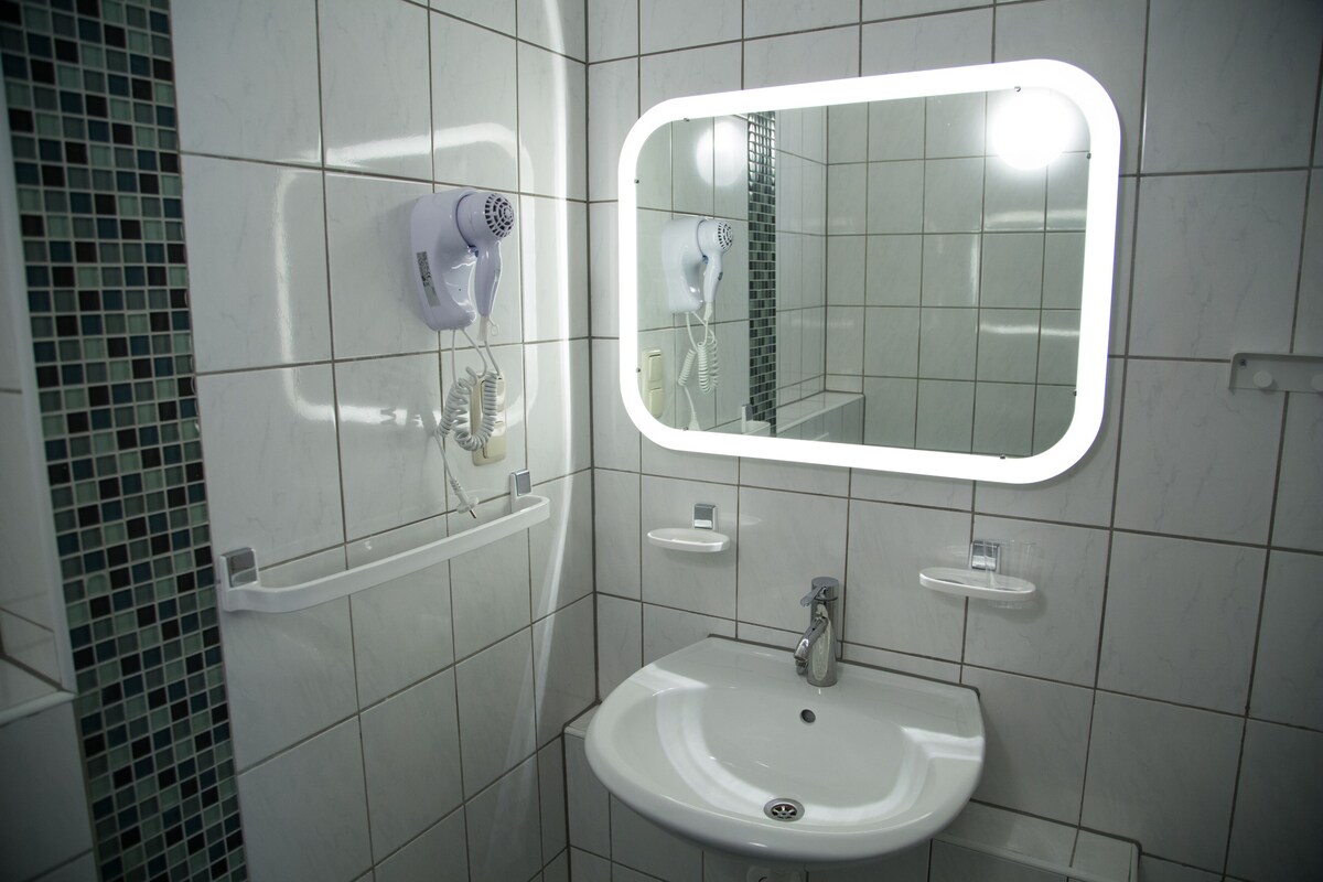 Une salle de bain avec un lavabo blanc, un miroir et un sèche-cheveux fixé au mur.