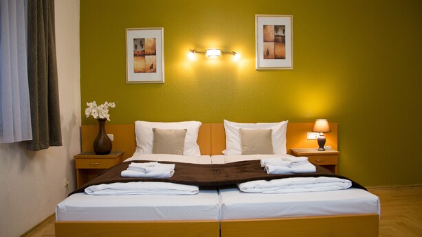 A double bed with white linens, a brown throw blanket, and two nightstands with lamps. - Garni Hotel Rödelheimer Hof (Frankfurt)