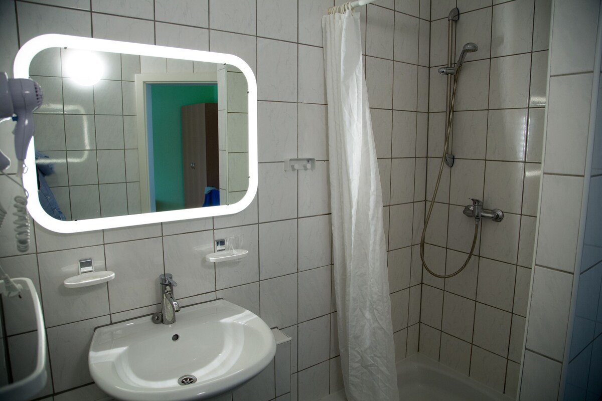 Une salle de bain avec un lavabo blanc, un miroir, une douche avec un rideau et un sèche-cheveux.