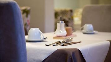 A dining table set with white plates, silverware, and a white vase.