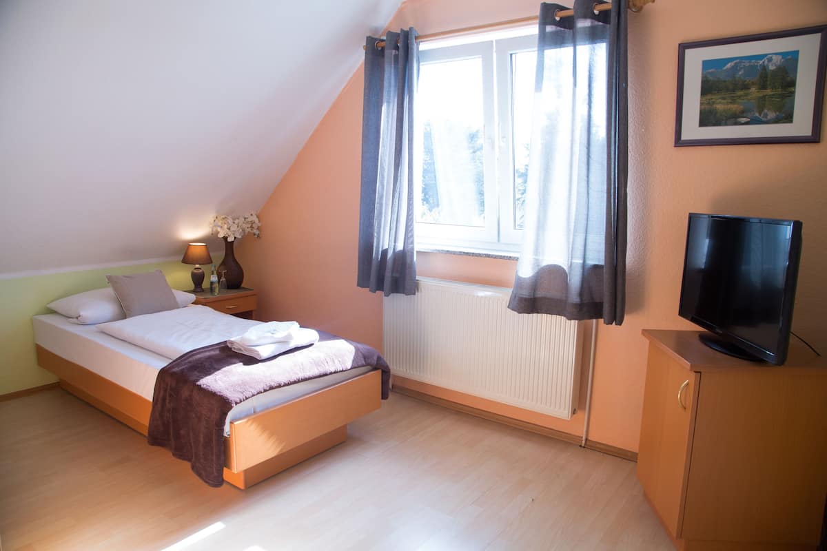 Een slaapkamer met een bed, nachtkastje, lamp, televisie en raam met gordijnen.