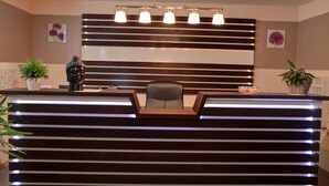 A reception desk with a modern design, featuring horizontal wooden slats and integrated lighting. There are two potted plants on either side of the desk, and a chair is positioned behind it. - Garni Hotel Rödelheimer Hof (Frankfurt)