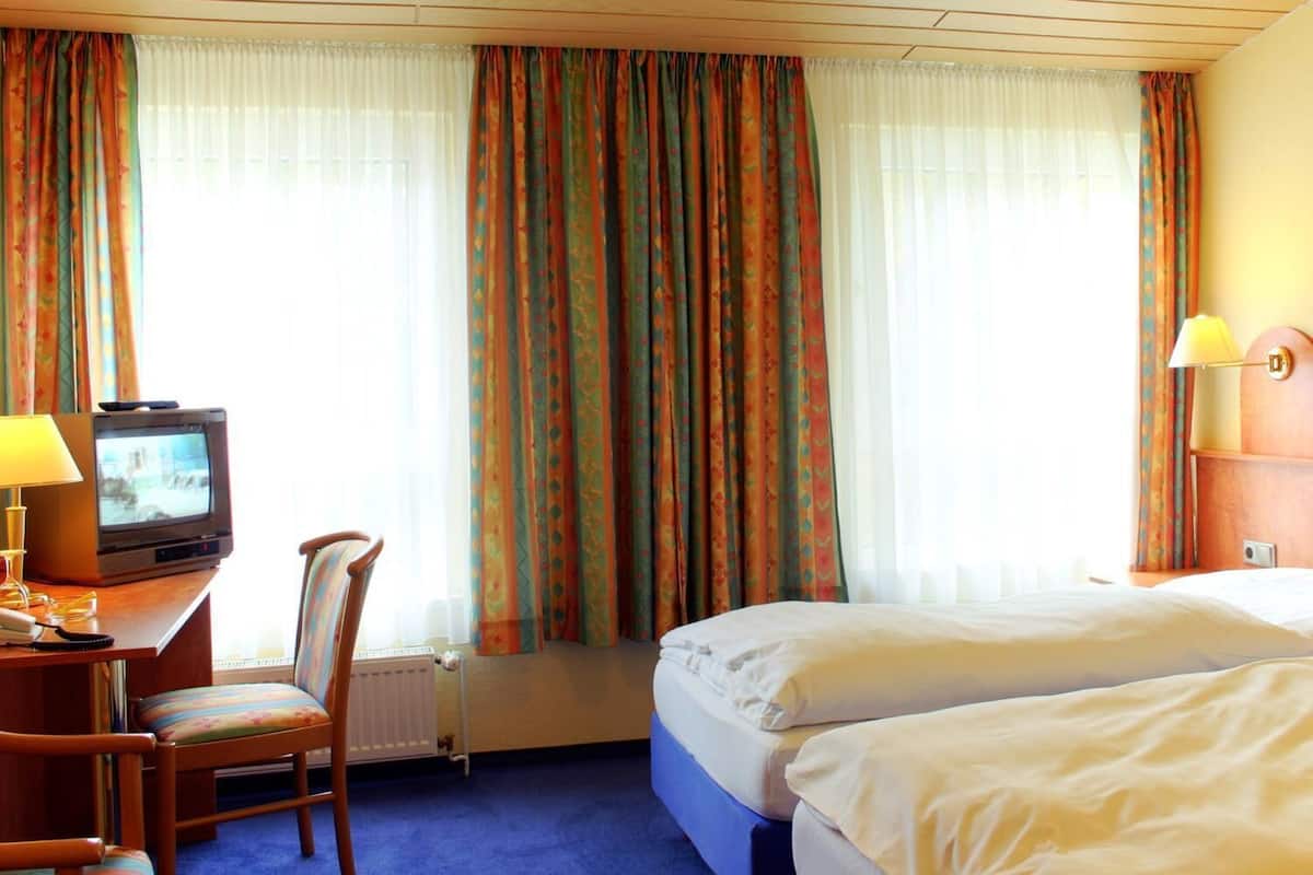 Una habitación de hotel con una cama, un escritorio con televisor, una silla y una lámpara.